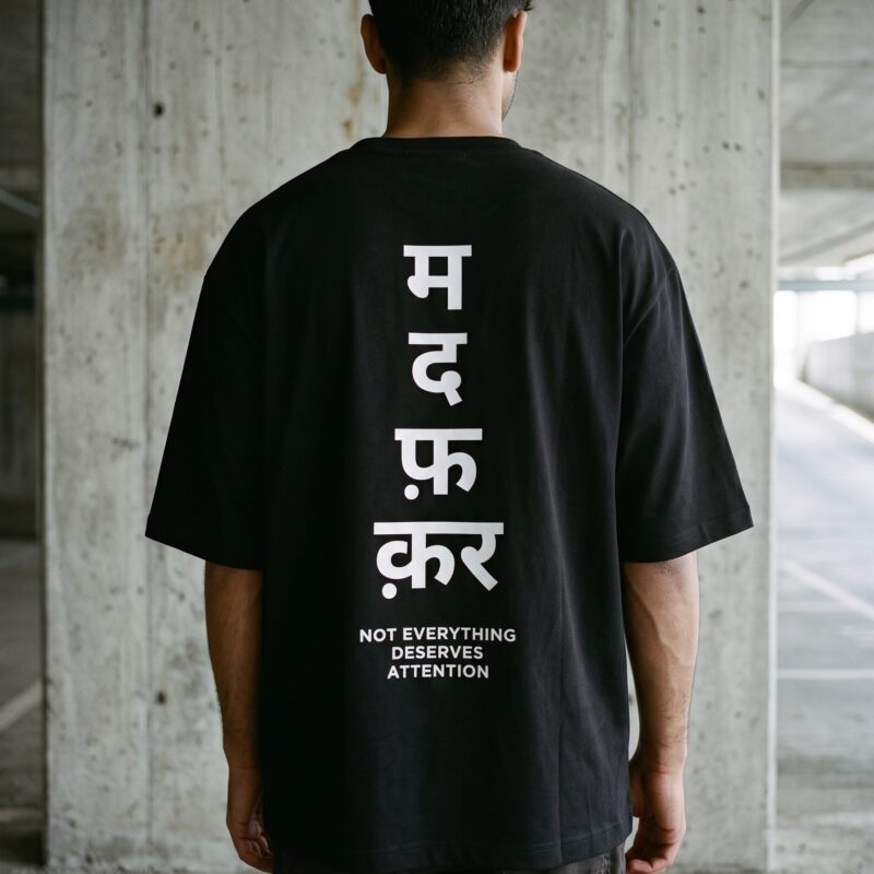 Rear view of MDFKR oversized black t-shirt featuring large Hindi typography graphic and Not Everything Deserves Attention slogan